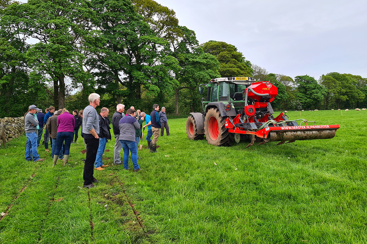 Group of people stood in a field looking at a tractor with a machine on the back for cutting furrows in the ground