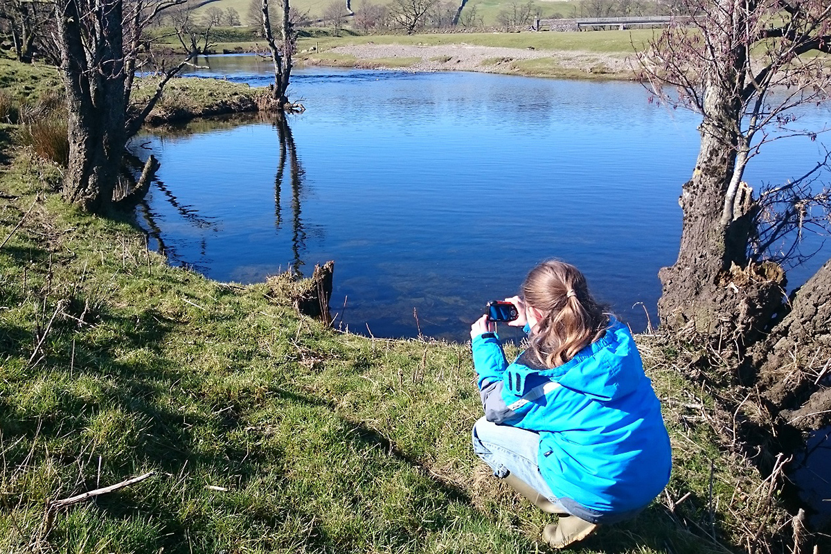 Girls taking photograph of the reflection of trees in the river