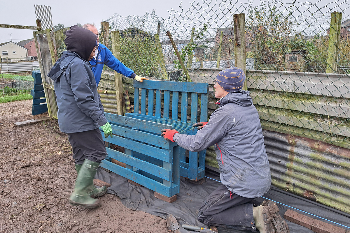 Three people building a potting bench using wooden pallets
