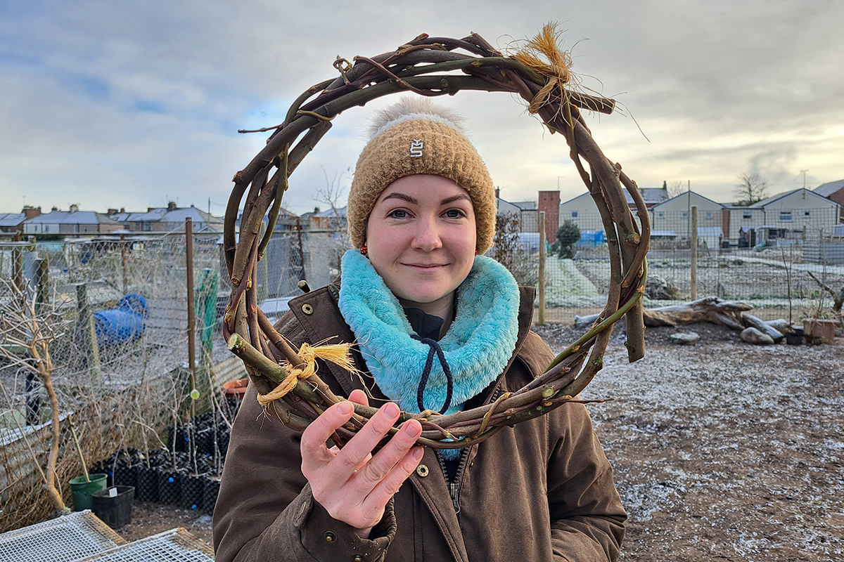 A woman holds up a round wreath made from willow woven into a circle.