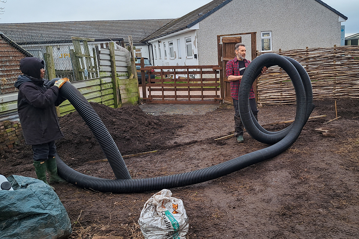 Two people in wet weather gear holding either end of a giant plastic tube