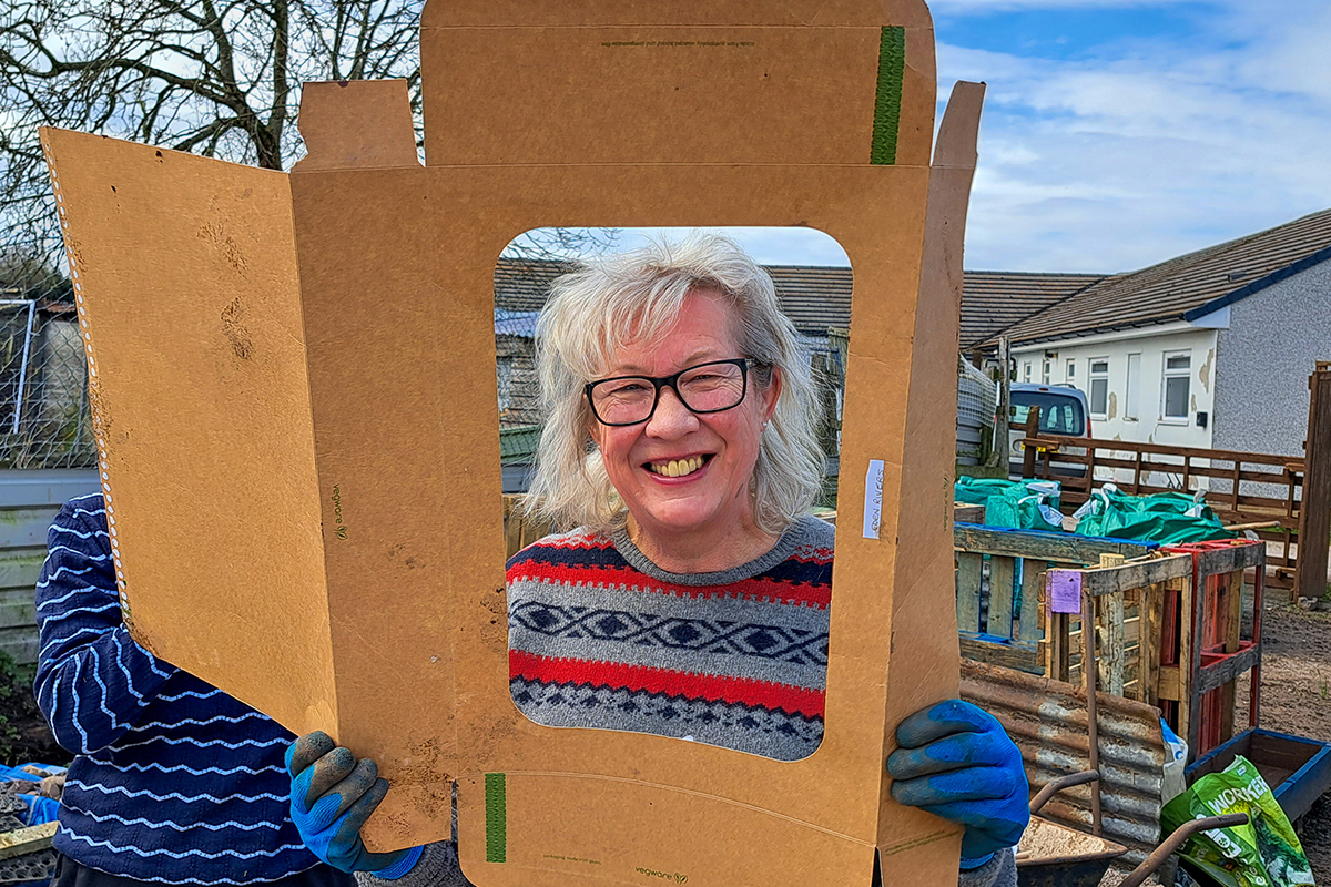 Woman with her head through a hole cut out of a flattened cardboard box