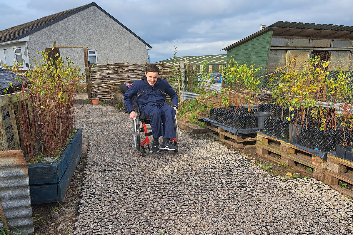 A wheelchair user wheeling himself along a flat, gravel path at the tree nursery.