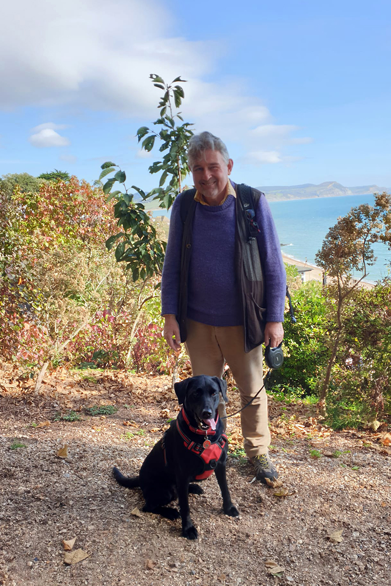 A man standing with his black dog sat next to him