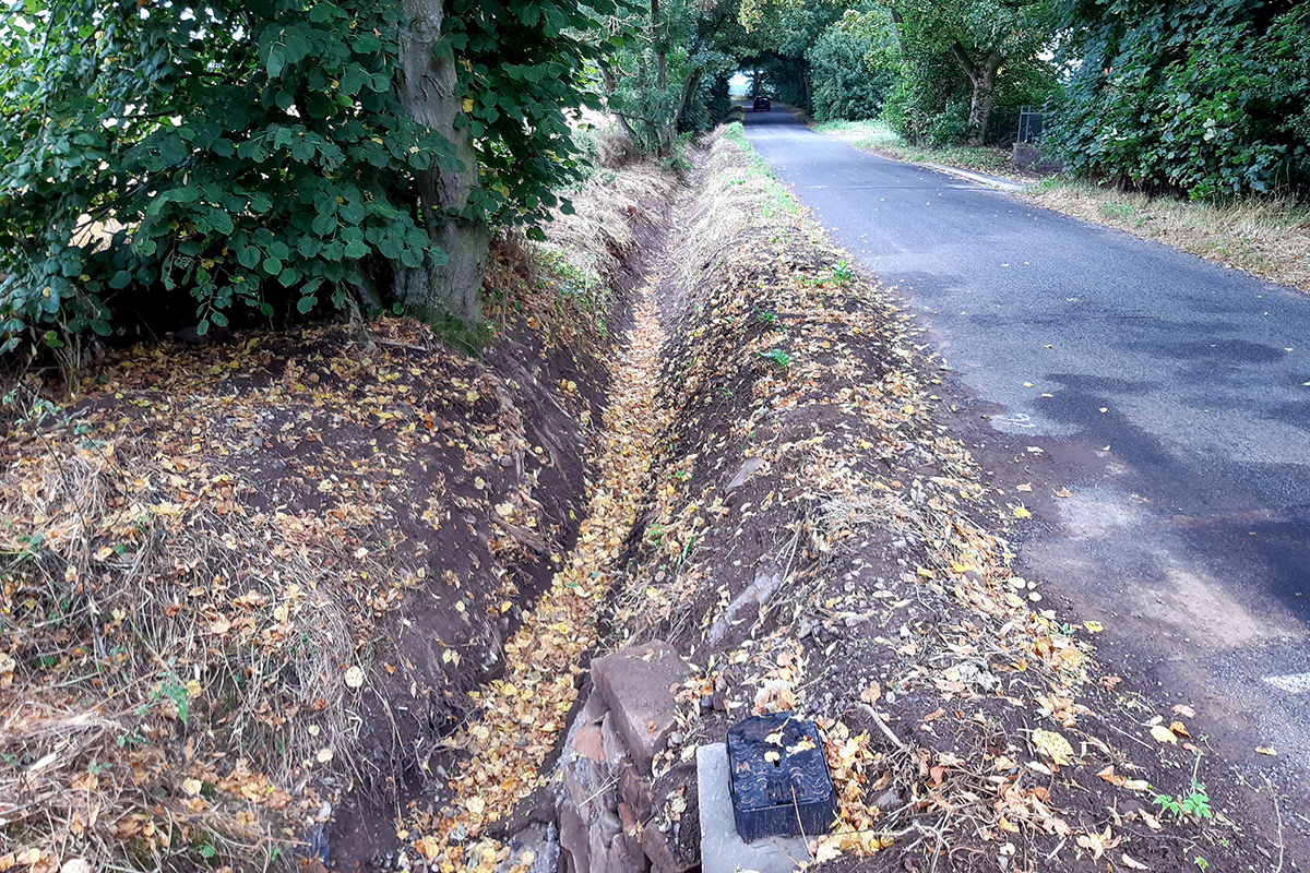 Newly dug ditch and improved culvert beside a road.
