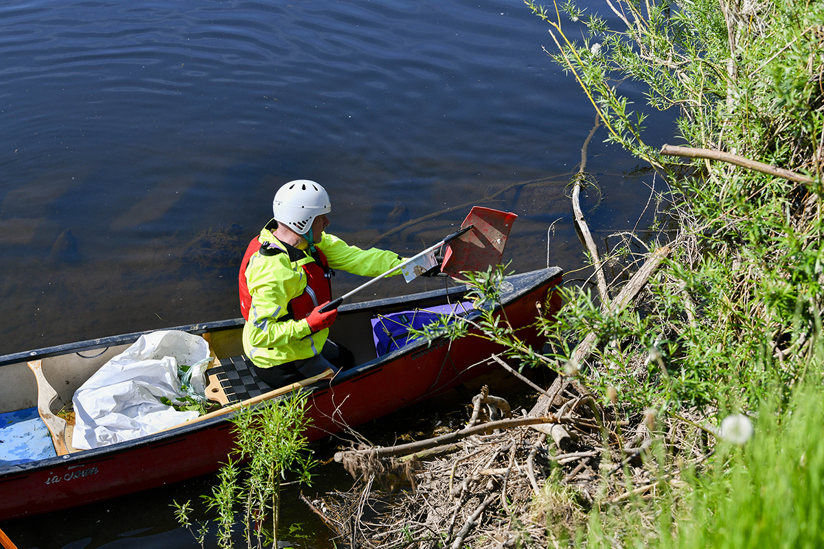 A man, sat in a canoe picking out rubbish from the riverbank