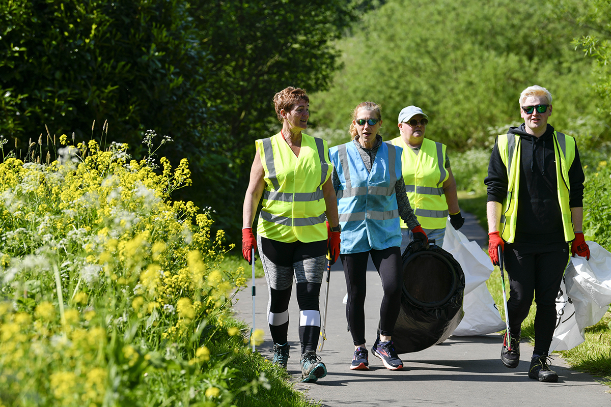 Four people wearing hi-viz vests walking along the path with bin bags and litter pickers.