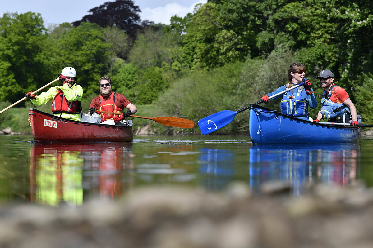 Two canoes on the river, each with two people paddling