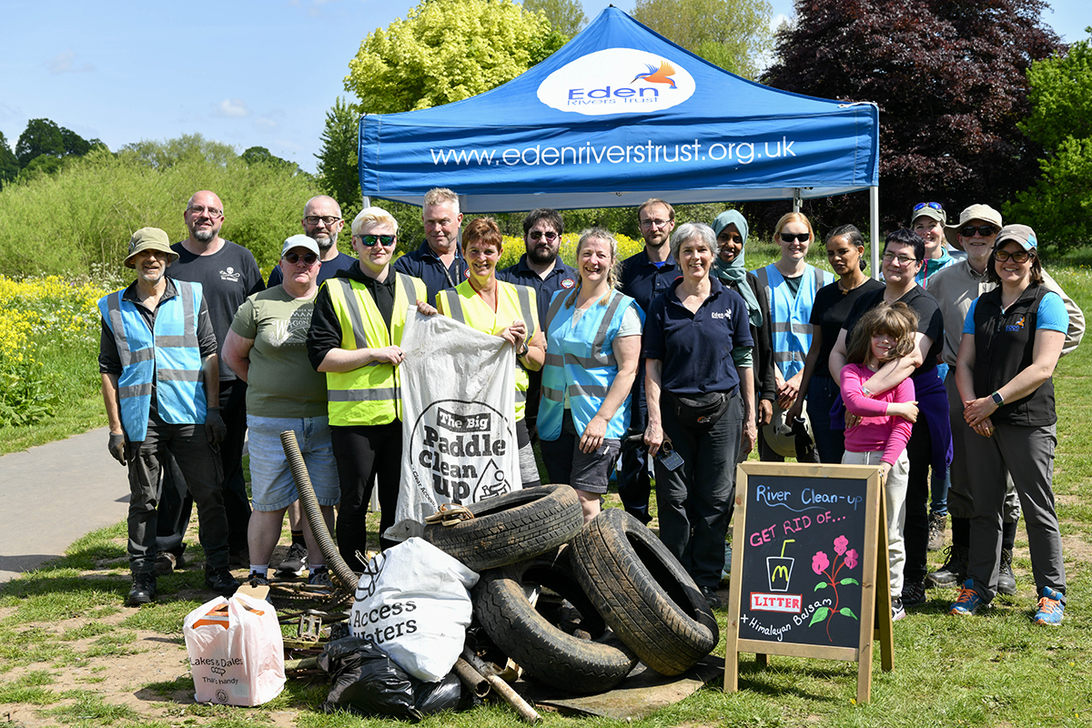 A large group of people standing in front of a pile of rubbish bags and tyres.