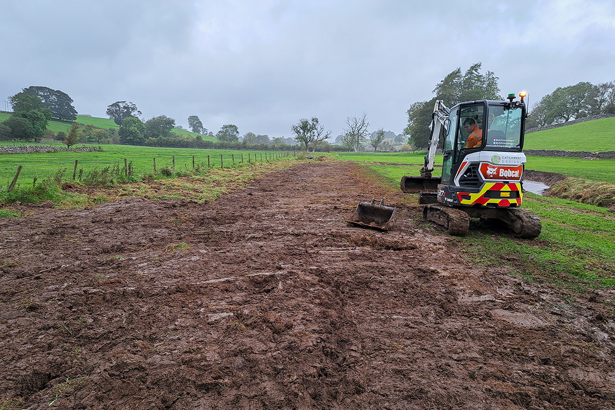 Digger next to a long line of brown earth - new turf to cover the river channel that has been filled in.