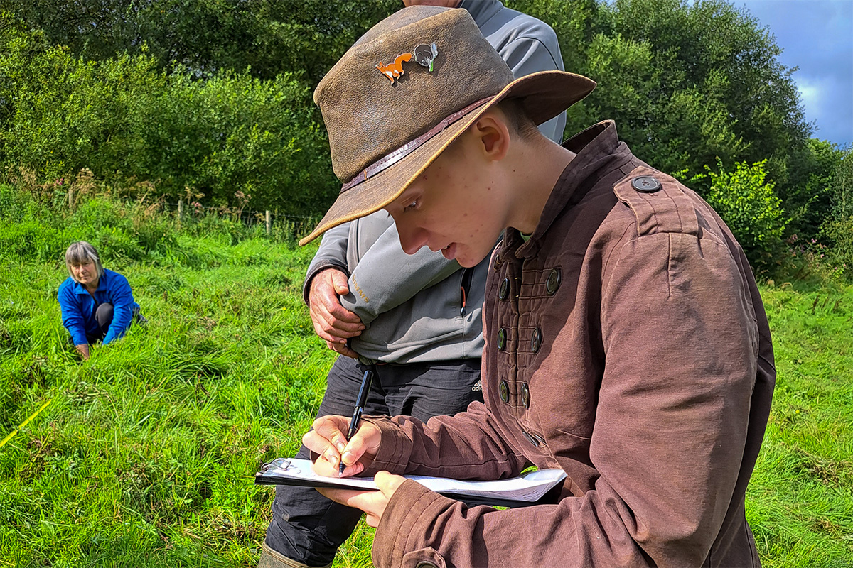 Close up of a person in a field. They are writing something on a clipboard.