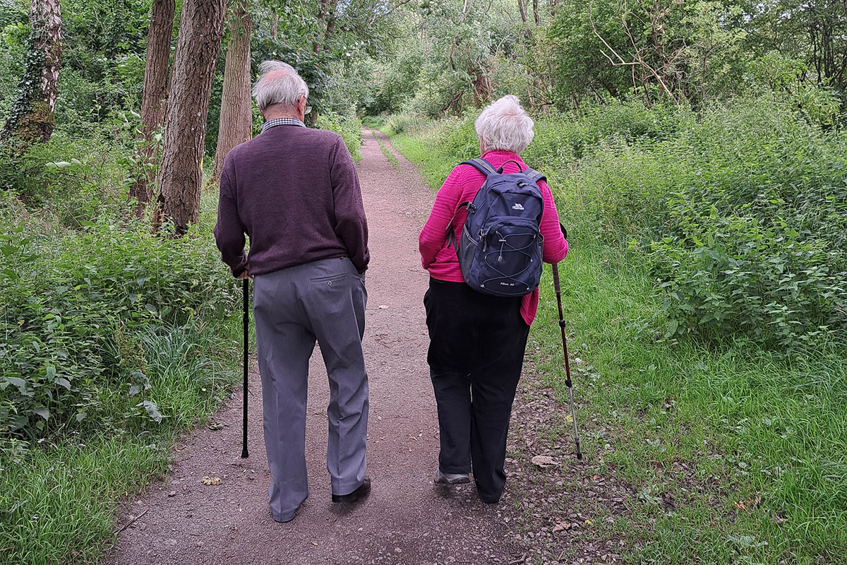 Two older people with walking poles, walking down a country away from the caemera.